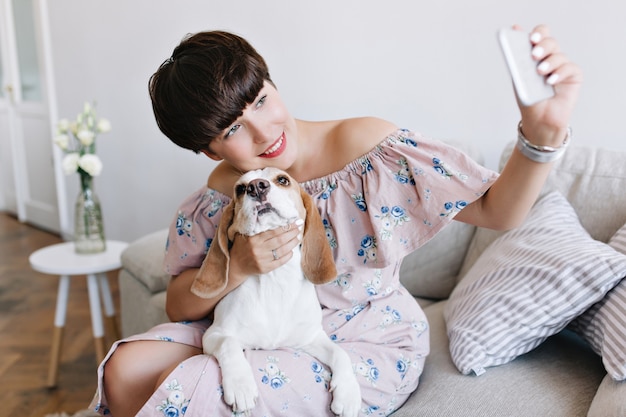 Free photo lovely young woman with nude makeup touching with love her beagle dog and taking picture of herself