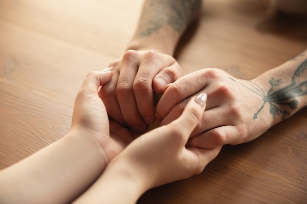 Free photo loving caucasian couple holding hands close-up on wooden wall.