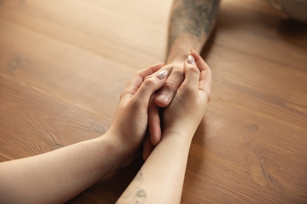 Free photo loving couple holding hands close-up on wooden desk