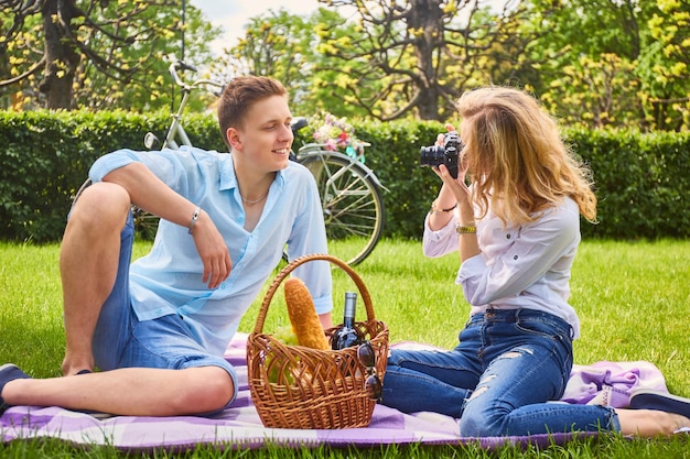 Free photo loving couple on a picnic in a park. blonde female photo shooting her boyfriend.