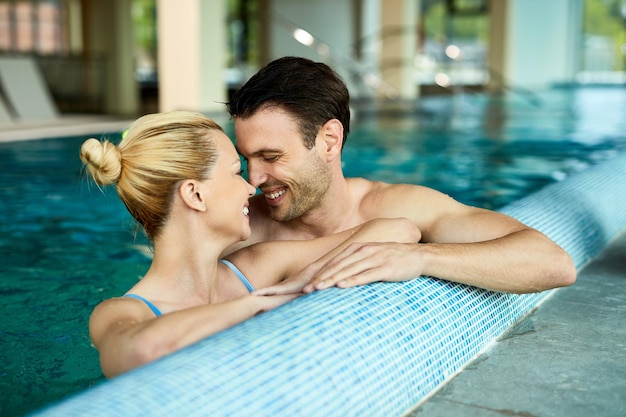 Loving couple talking face to face while being in the water of indoor swimming pool at the spa