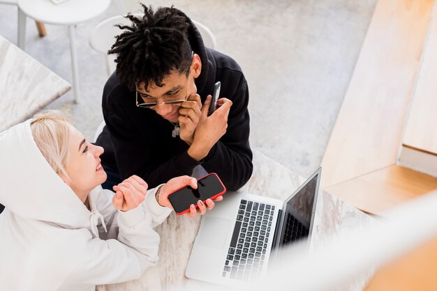 Loving smiling interracial couple holding mobile phone in hands looking at each other