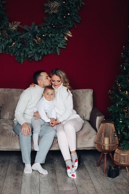 Loving young parents sitting on couch and kissing while holding a kid between them