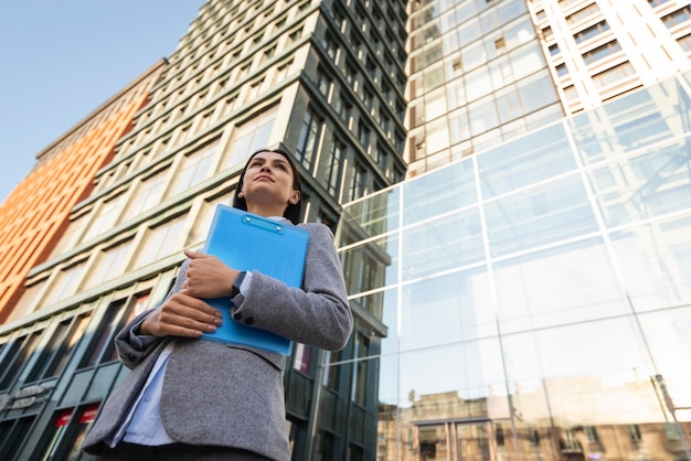 Free photo low angle of businesswoman holding clipboard in the city