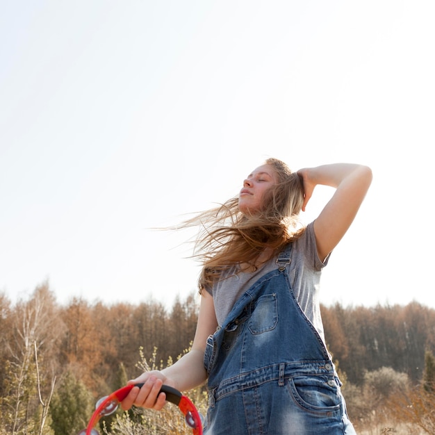 Free photo low angle of of carefree woman in nature holding tambourine