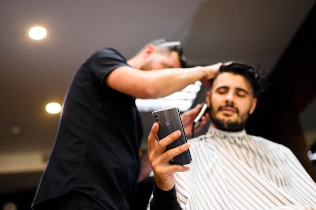 Low angle costumer at barber shop checking his phone