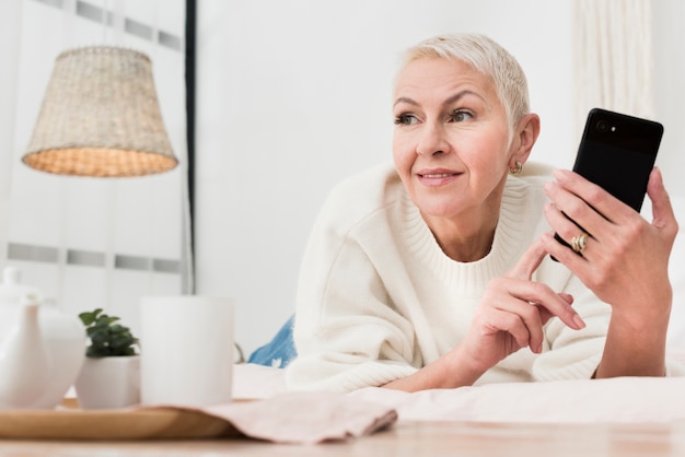 Free photo low angle of elderly woman in bed holding smartphone