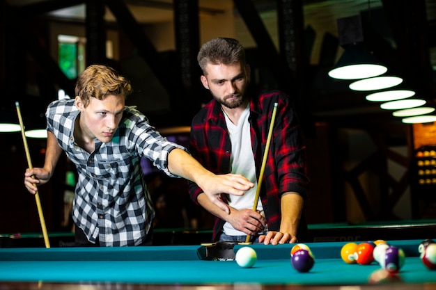 Free photo low angle guys with pool cues playing billiard