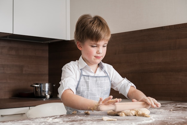 Free photo low angle little boy at home rolling dough