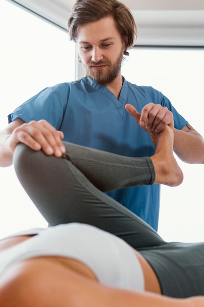 Low angle of osteopathic therapist checking female patient's leg movement