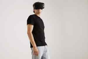 Free photo low angle portrait of a man wearing vr headset, blank black t-whirt and jeans looking around isolated on white