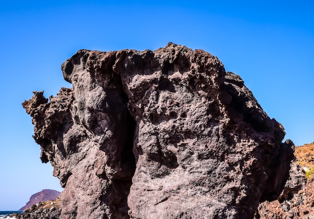 Free photo low angle shot of a big rock on a beach with a clear blue sky