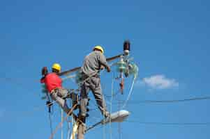 Free photo low angle shot of electric linemen working on pole