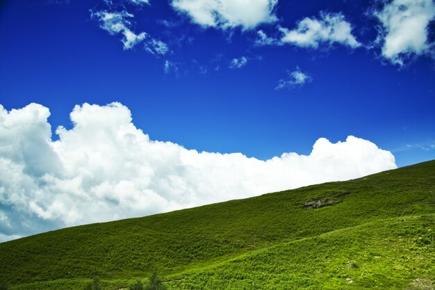 Low angle shot of a green hill with a cloudy blue sky in the background