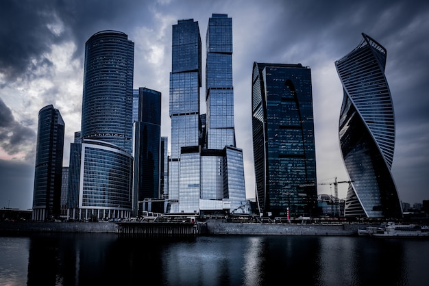 Free Photo low angle shot of grey skyscrapers in front of the river under the dark cloudy sky