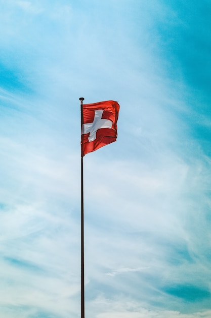 Free photo low angle shot of switzerland flag on a pole under the breathtaking cloudy sky