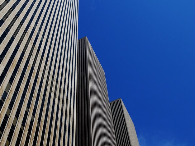 Low angle shot of three identical skyscrapers under the bright blue sky