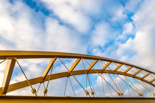 Free photo low angle shot of a yellow cable-stayed bridge with a blue cloudy sky