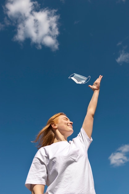 Low angle smiley woman holding face mask