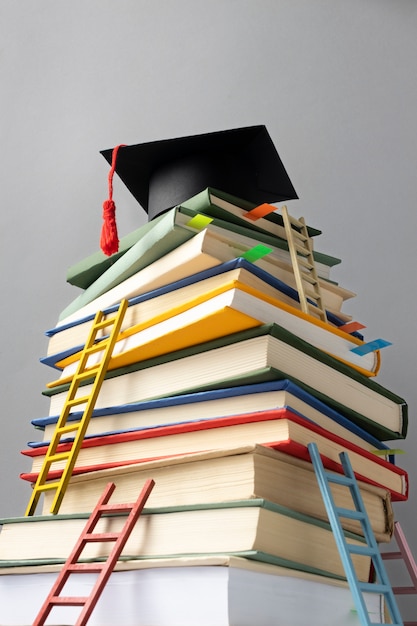 Free photo low angle of stacked books, a graduation cap and ladders for education day