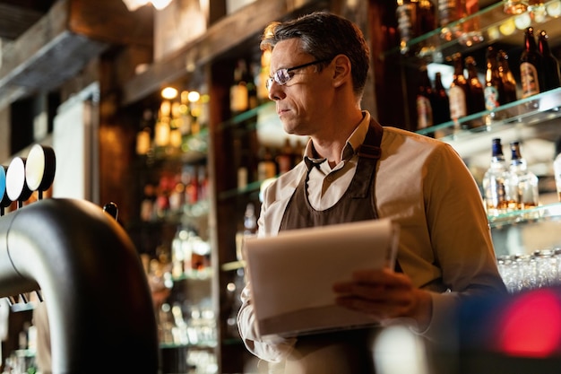 Free photo low angle view of bartender going through inventory list while working in a pub.