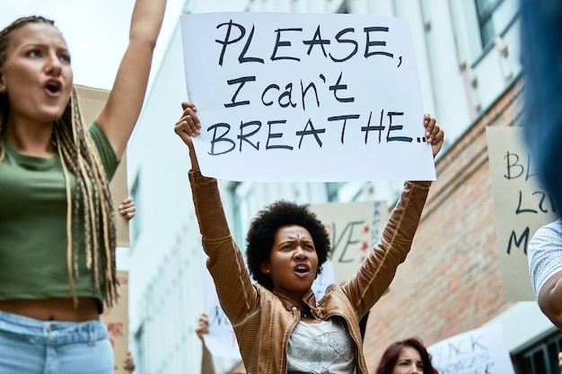 Free photo low angle view of a black woman holding banner with i can't breathe inscription while demonstrating for human rights with crowd of people