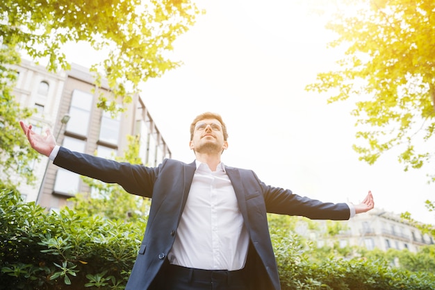 Free Photo low angle view of a businessman standing in front of building outstretching his arms