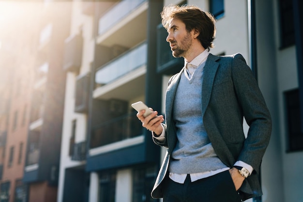 Low angle view of businessman using mobile phone while standing on the street and looking away.