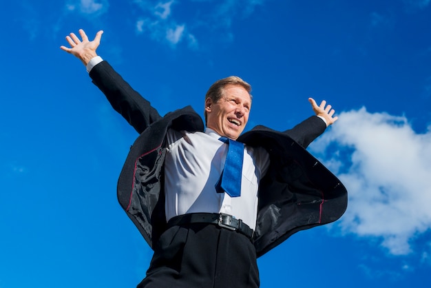 Free photo low angle view of an excited businessman raising his arms against sky