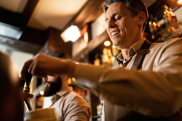 Free photo low angle view of happy barista pouring draft beer while working in a pub.