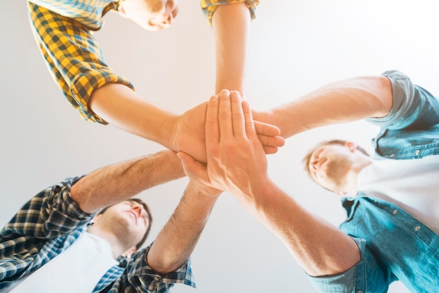 Low angle view of male friends stacking hands against white background