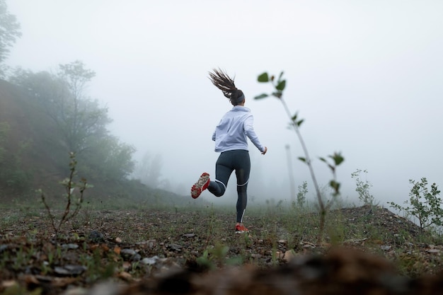 Low angle view of motivated sportswoman running in nature during misty weather Copy space