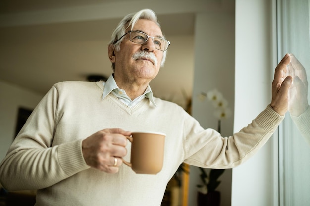 Low angle view of senior man day dreaming while drinking coffee and looking through the window