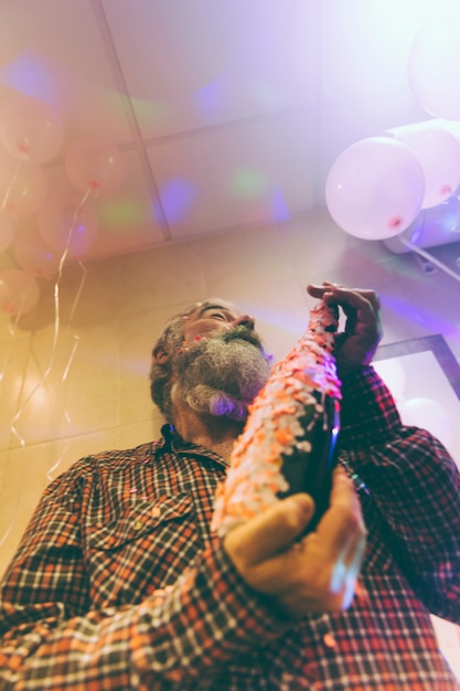 Low angle view of senior man holding alcohol bottle in hand decorated with confetti