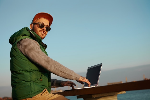 Free photo low angle view of trendy looking fashionable young man with stubble using generic electronic gadget