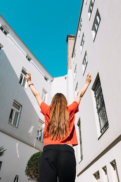 Free photo low angle view of a woman raising her arms near residential building