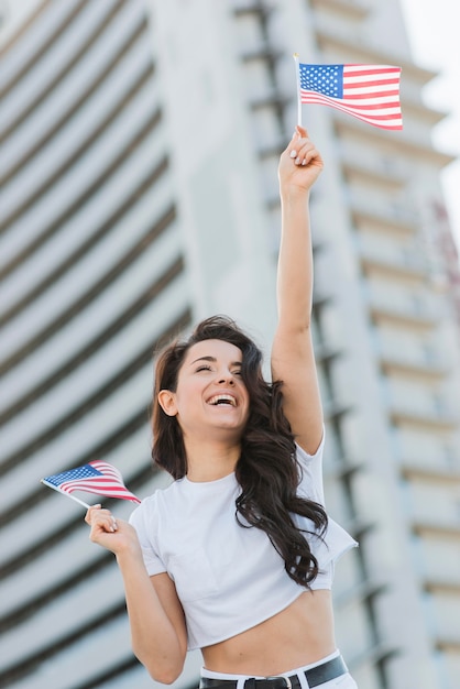 Low angle woman holding two usa flagsand smiling