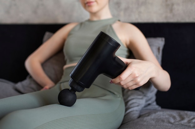 Free Photo low angle woman using massage gun on leg