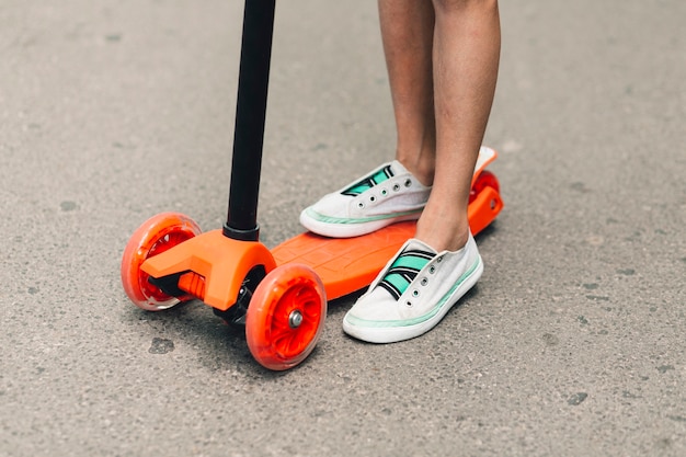 Low section of a girl standing on an orange push scooter at street