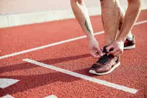 Free photo low section of male athlete on the start line tying his shoelace on running track