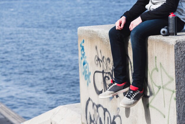 Low section of a man sitting on graffiti wall with aerosol can