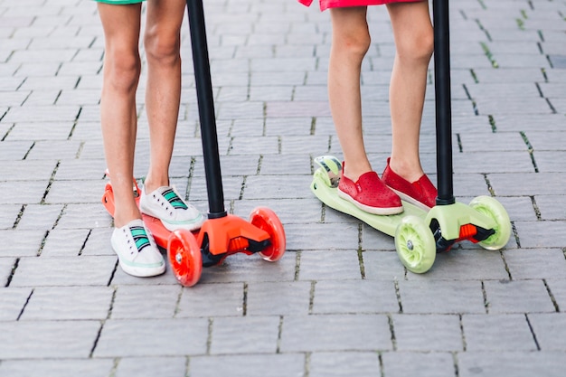 Free photo low section of two girls standing on kick scooter