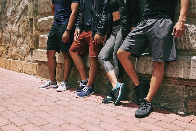 Free photo low section of unrecognizable people in activewear standing at the wall of a building