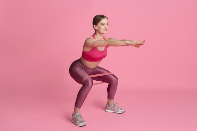 Lower body. Beautiful young female athlete practicing in studio, monochrome pink portrait.