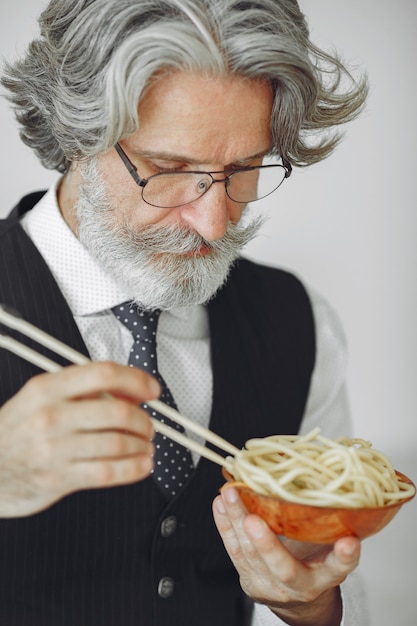 Free photo lunch break. elegant man in office. businessman in white shirt. man eats noodles.