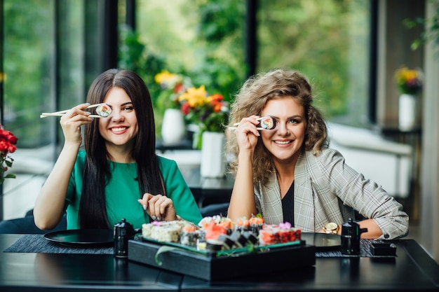 Free Photo lunch at a chinese restaurant on the summer terrace. two sistres  eat sushi with chinese sticks.