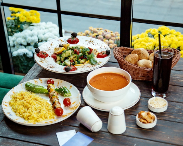 A lunch setup with rice and chicken skewers greek salad and lentil soup