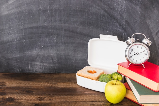 Lunchbox and apple near books and alarm clock