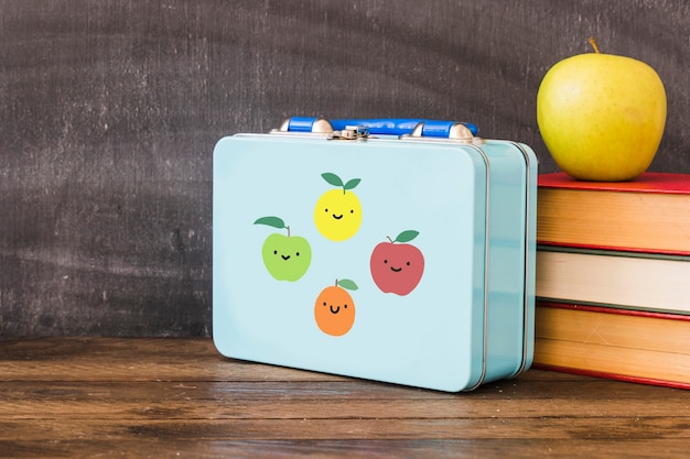 Lunchbox near stack of books and apple