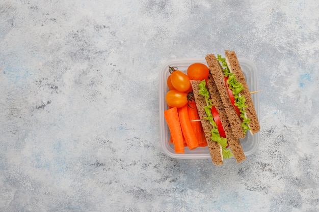 Lunchbox with sandwich, vegetables, fruit on white .